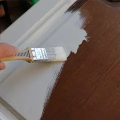 Application d'un vernis après peinture sur un meuble en bois. La main tient un pinceau pour appliquer la couche protectrice.