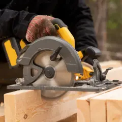 Main d'un bricoleur utilisant une scie circulaire pour couper du bois. La scie a une hauteur de coupe de 200 mm.