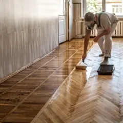 Un homme applique du vitrificateur sur un parquet. Le temps de séchage vitrificateur est crucial pour un résultat parfait.