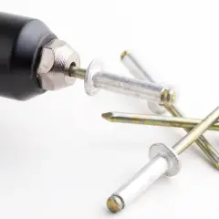 Un outil noir est prêt à fixer un type de rivet aveugle. Plusieurs rivets sont éparpillés sur la surface blanche.