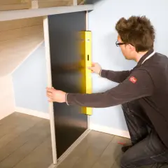Un homme utilise un niveau pour fabriquer un placard sous pente de toit.
