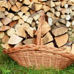 Panier en osier rempli de bois de chauffage, prêt pour le traitement du bois contre l'humidité. Le fond est un mur de bûches empilées.