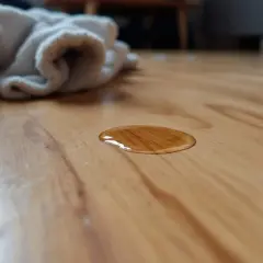 Une flaque de liquide brun sur un parquet en bois. Un tissu blanc est en arrière-plan. Comment enlever tache incrustée parquet ?