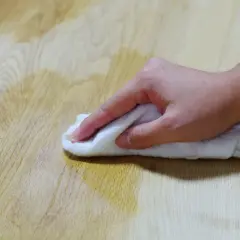 Main d'une personne essuyant une tache d'huile sur un parquet en bois avec un chiffon blanc.