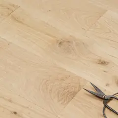 Un parquet en chêne clair, avec des ciseaux posés dessus. Peut-on laisser un parquet brut ? La réponse est oui, pour un style naturel.