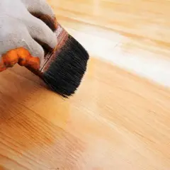 Main gauche gantée appliquant de l'huile de lin sur du bois. Attention, l'huile de lin peut présenter un danger d'auto-inflammation si mal stockée.