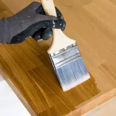 Application d'huile de lin au pinceau sur un plateau en bois. La finition protège et sublime le grain du bois.