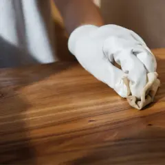 Main d'une personne portant un gant blanc appliquant de l'huile de lin dure naturelle sur un meuble en bois.