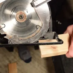Démonstration de comment utiliser une scie circulaire pour couper du bois. La lame est prête à entamer le morceau de bois tenu par une main.