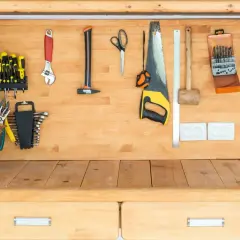 Un établi en bois bien rangé avec des outils : tournevis, clés, scie, marteau, ciseaux, et une boîte de forets.
