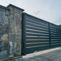 Portail coulissant moderne en aluminium anthracite, juxtaposé à un mur en pierres naturelles. Le portail est en pose, prêt à sécuriser l'entrée.