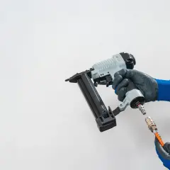 Main d'un bricoleur connectant un tuyau à un pistolet à clous pneumatique, un outil essentiel pour tout projet de menuiserie.