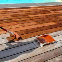 Application d'un saturateur sur une terrasse en bois exotique. Le rouleau dépose le produit, redonnant vie au bois.