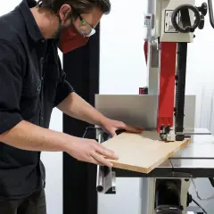 Un artisan utilise une scie à ruban, un des outils pour couper le bois, pour façonner une planche.
