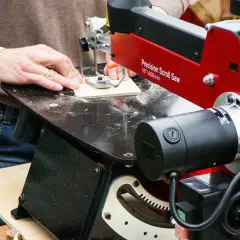 Un artisan utilise une scie à chantourner pour découper des formes complexes dans du bois. Cet outil permet de réaliser des détails fins et précis.