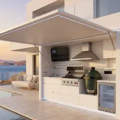 Une cuisine d'été fait maison moderne avec barbecue, évier, frigo et TV, surplombant la mer et une piscine.