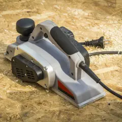 Une raboteuse électrique, prête à aplanir le bois, repose sur un chantier jonché de copeaux.