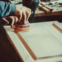 Un artisan utilise une ponceuse orbitale pour lisser une porte en bois. Le choix de la ponceuse est crucial pour un travail de finition parfait.
