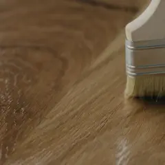 Application d'un vernis ou huile pour bois avec un pinceau sur une surface en bois.