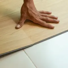 Pose d'un parquet stratifié imitation bois clair. Une main ajuste une lame sur un sol blanc.