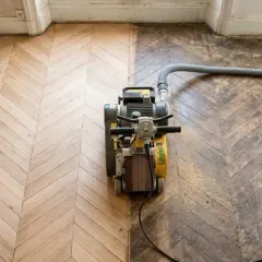 Ponçage d'un parquet ancien en chevrons, révélant sa beauté. Le prix du ponçage parquet dépend de l'état. Aspirateur industriel en action.