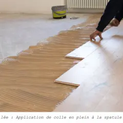 Pose de parquet collé : application de colle en plein à la spatule crantée, avant la pose des lames de bois.
