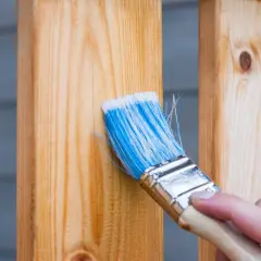 Maintenir le bois avec une lasure ou un vernis : une main applique un produit sur des lattes de bois.