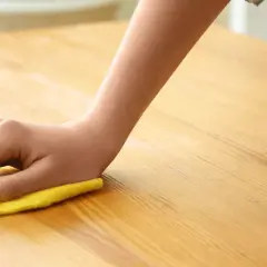 Main d'enfant nettoyant une table en bois avec un chiffon jaune. Apprenez comment nettoyer une table en bois pour un éclat parfait.