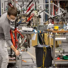 Un ouvrier assemble un vélo rouge, peut-être une création de la marque Korman, dans un atelier rempli de cadres.