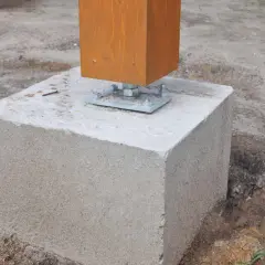 Un poteau en bois est fixé sur un plot béton à enterrer, prêt pour une construction solide.