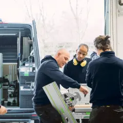 Des artisans discutent d'un outil Festool, l'origine de leur savoir-faire, devant un fourgon aménagé.