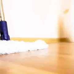 Une serpillère blanche et moelleuse nettoie un parquet brillant. La lumière douce éclaire la scène, créant une ambiance chaleureuse.
