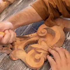 Un artisan utilise un ciseau pour sculpter le bois, créant des volutes complexes sur une pièce ornementale.