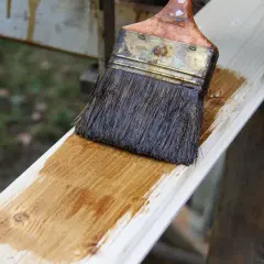 Application d'une lasure effet bois blanchi sur une planche de bois clair. Le pinceau dépose une fine couche de produit.