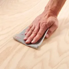 Main d'artisan effectuant un égrenage sur une surface en bois clair avec du papier de verre P100.