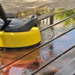 Nettoyer terrasse bois savon noir : un nettoyeur haute pression jaune et noir en action sur des lattes de bois mouillées.