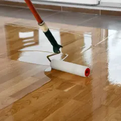 Application d'une première couche de vitrificateur sur un parquet en bois. Le rouleau laisse une surface brillante et humide.