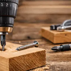 Apprenez comment utiliser une perceuse pour visser dans le bois. Une mèche est dans le bois, une vis à côté.