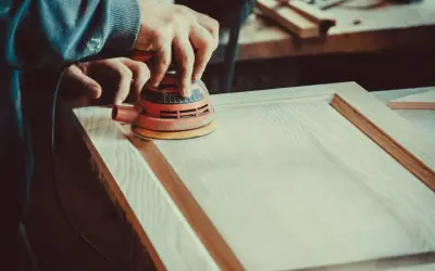 Un artisan utilise une ponceuse orbitale pour lisser une porte en bois. Le choix de la ponceuse est crucial pour un travail de finition parfait.