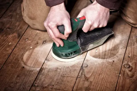 Mains tenant une ponceuse pour le ponçage du parquet. La poussière vole autour de l'outil pendant le travail.