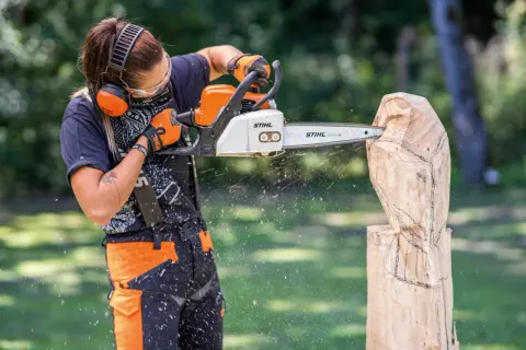 Artiste créant une sculpture bois tronçonneuse facile, des copeaux volent.