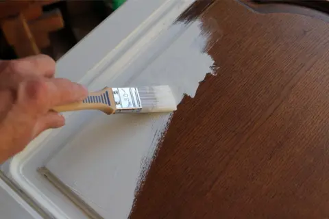Application d'un vernis après peinture sur un meuble en bois. La main tient un pinceau pour appliquer la couche protectrice.