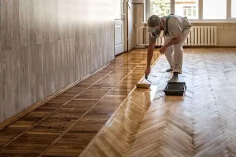 Un homme applique du vitrificateur sur un parquet. Le temps de séchage vitrificateur est crucial pour un résultat parfait.