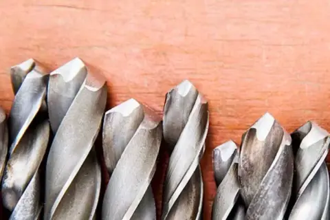 Ensemble de forets métalliques sur fond de bois. Apprenez comment mettre un foret dans une perceuse pour vos projets.