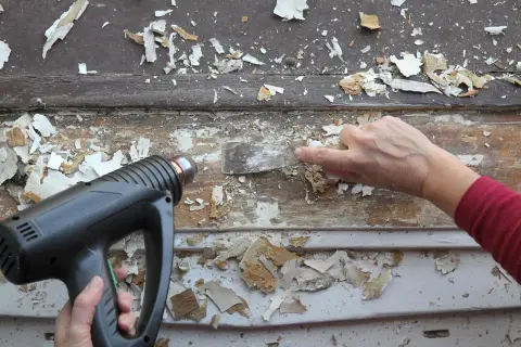 Un décapeur thermique avec réglage de température est utilisé pour ramollir la vieille peinture avant de la gratter.