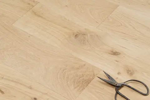 Un parquet en chêne clair, avec des ciseaux posés dessus. Peut-on laisser un parquet brut ? La réponse est oui, pour un style naturel.