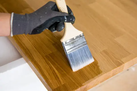 Application d'huile de lin au pinceau sur un plateau en bois. La finition protège et sublime le grain du bois.