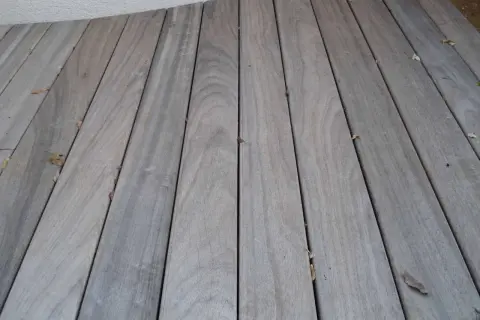 Planches de bois grisé, patinées par le temps, formant une terrasse. Quelques feuilles mortes parsèment le sol.