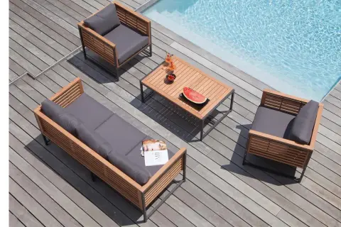 Salon de jardin en bois teck avec coussins gris, près d'une piscine. Table basse avec fruits et boissons.