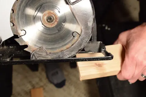 Démonstration de comment utiliser une scie circulaire pour couper du bois. La lame est prête à entamer le morceau de bois tenu par une main.